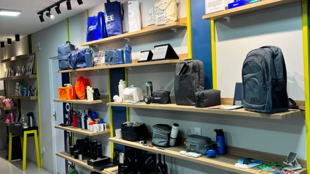 Prateleiras do showroom da Seven Gráfica com amostras de brindes, mochilas, copos e materiais corporativos personalizados